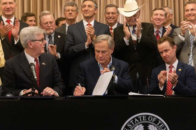 Governor Abbott signs second amendment legislation surrounded by a group of people. Image