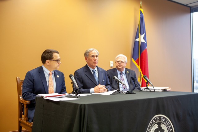 Governor Abbott gives remarks at a press conference while sitting between Representative Briscoe Cain and Senator Paul Bettencourt in Houston
